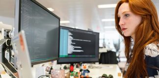 A female developer coding on dual monitors in a modern office, working on New Software RCSDASSK
