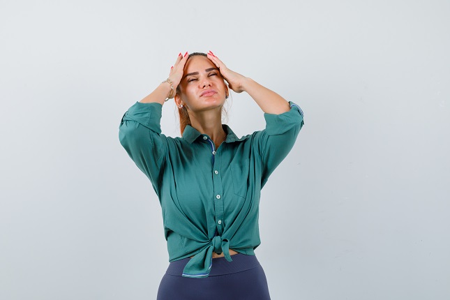 young lady in green shirt holding hands on head and looking tired , front view.