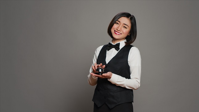 Woman hotel employee ringing front desk service bell in studio